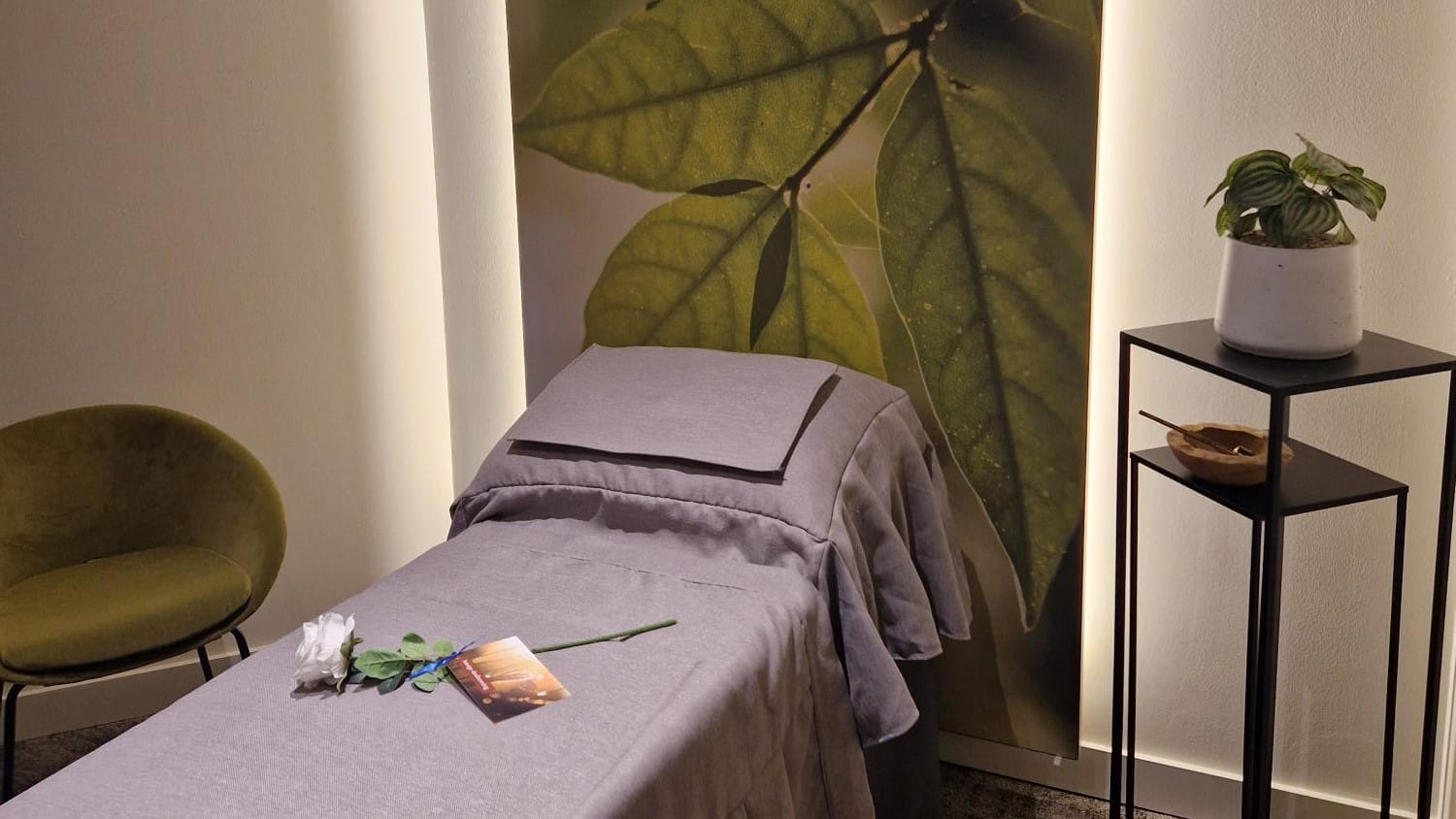 Groetkamer met lila ligbed, groene stoffen stoel ernaast en zachte verlichting